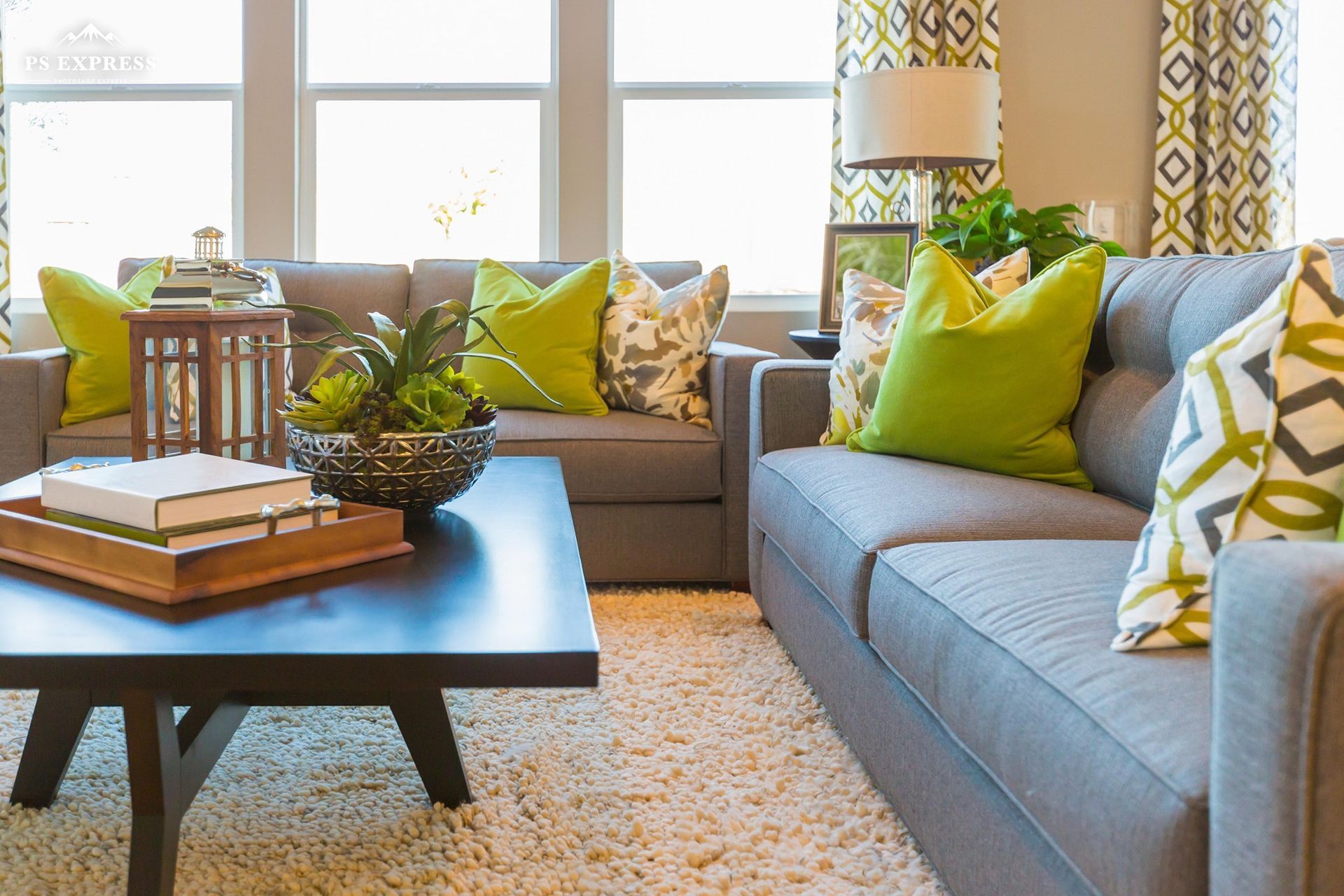 Bright living room with gray sofa, green pillows, coffee table, and large windows.
