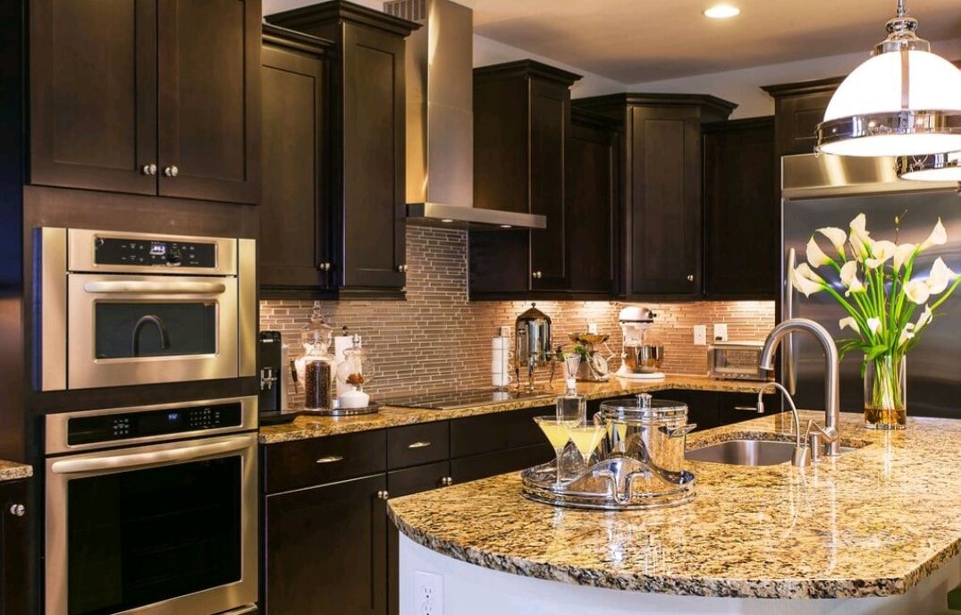Modern kitchen with dark wood cabinets, stainless appliances, and a granite island with flowers and glassware