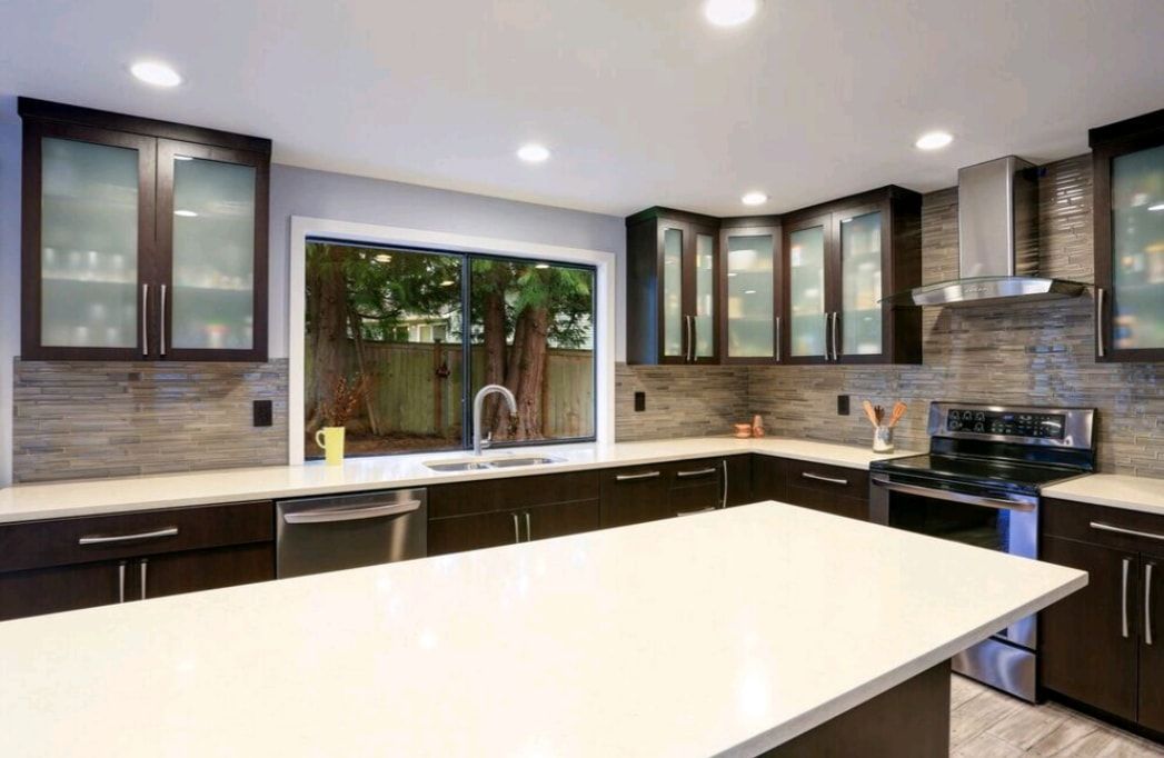 Modern kitchen with white island, dark cabinets, stainless stove, and large window over the sink