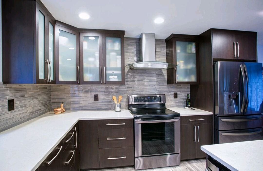Modern kitchen with dark wood cabinets, stainless steel appliances, white countertops, and gray tile backsplash