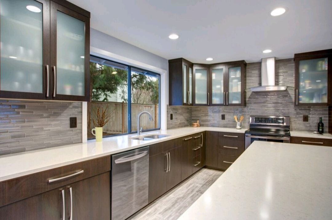 Modern kitchen with dark wood cabinets, stainless steel appliances, white countertops, and a large window