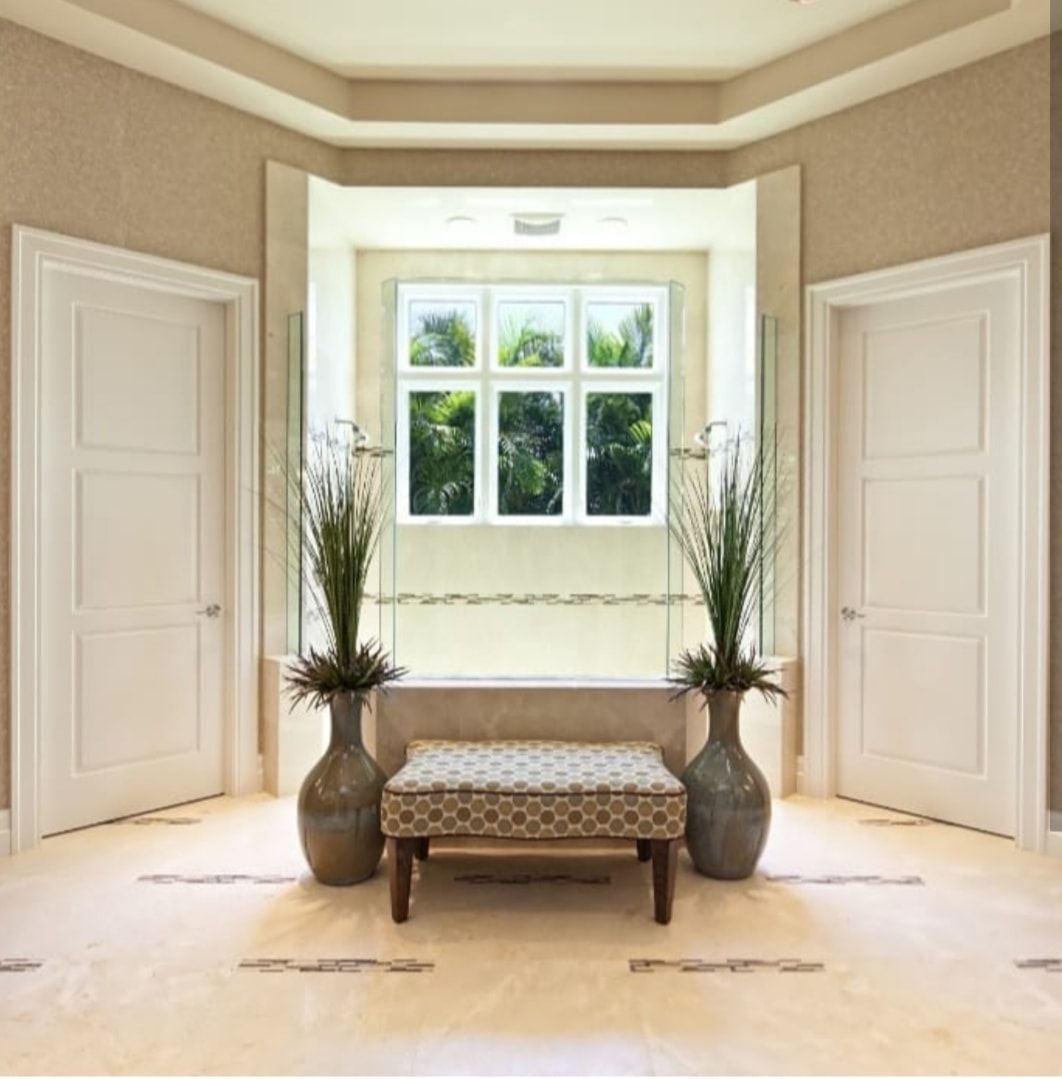 Bright hallway with a cushioned bench, large window, and matching vases with tall plants on both sides