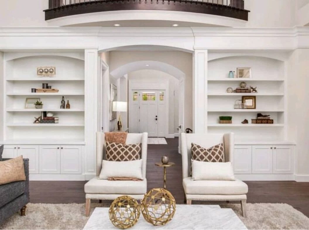 Bright white living room with built-in shelves, two armchairs, and gold decorative accents