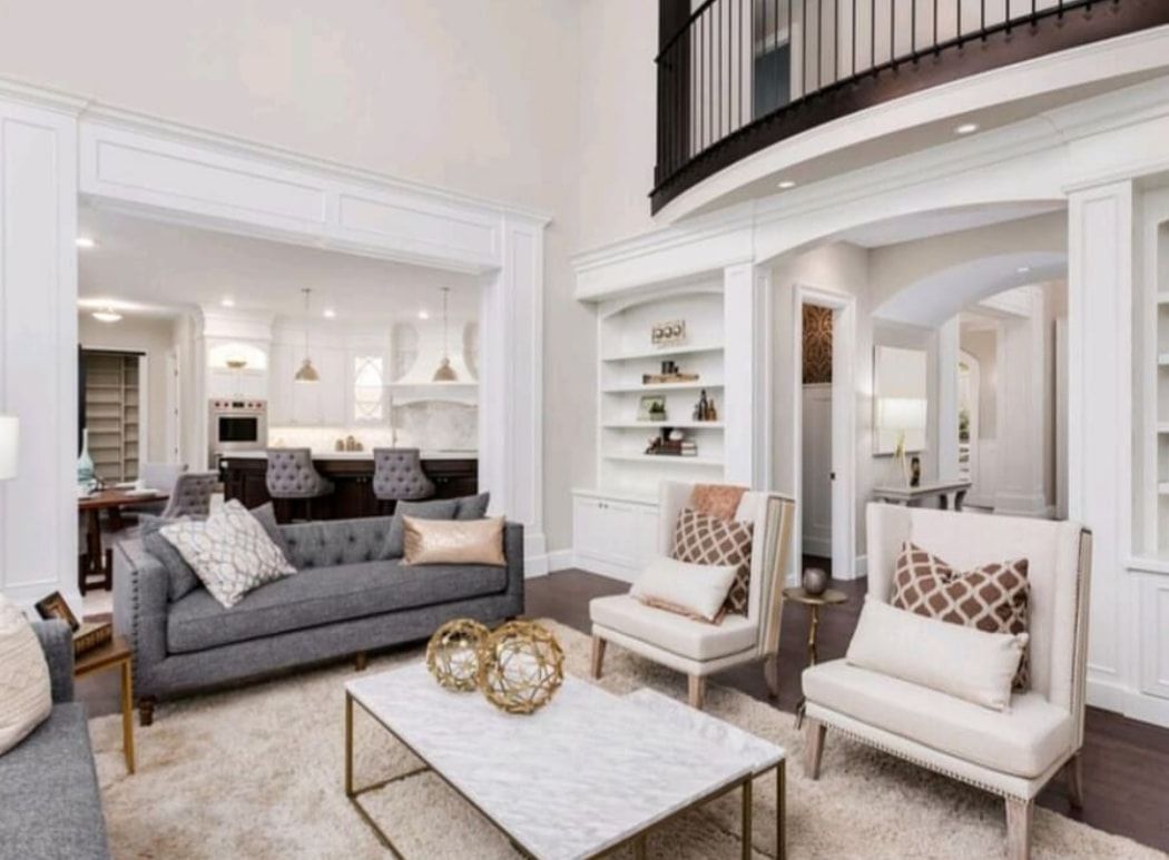 Bright modern living room with gray sofa, two beige chairs, white coffee table, and tall ceiling.