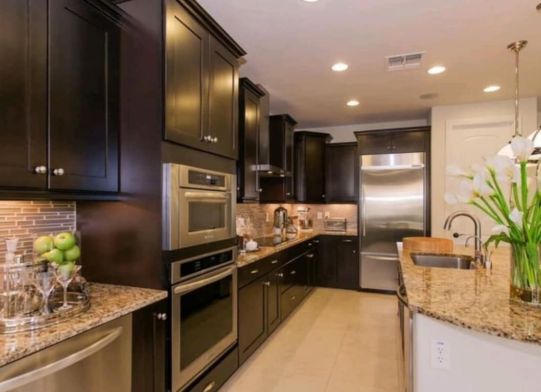 Modern kitchen with dark wood cabinets, granite countertops, stainless steel appliances, and a potted orchid
