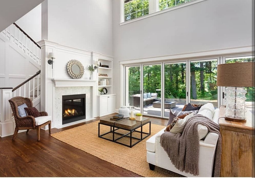 Bright living room with fireplace, white sofa, and large windows overlooking trees.
