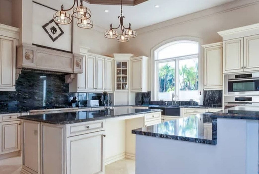 Bright white kitchen with black countertops, pendant lights, and a large window over the sink.