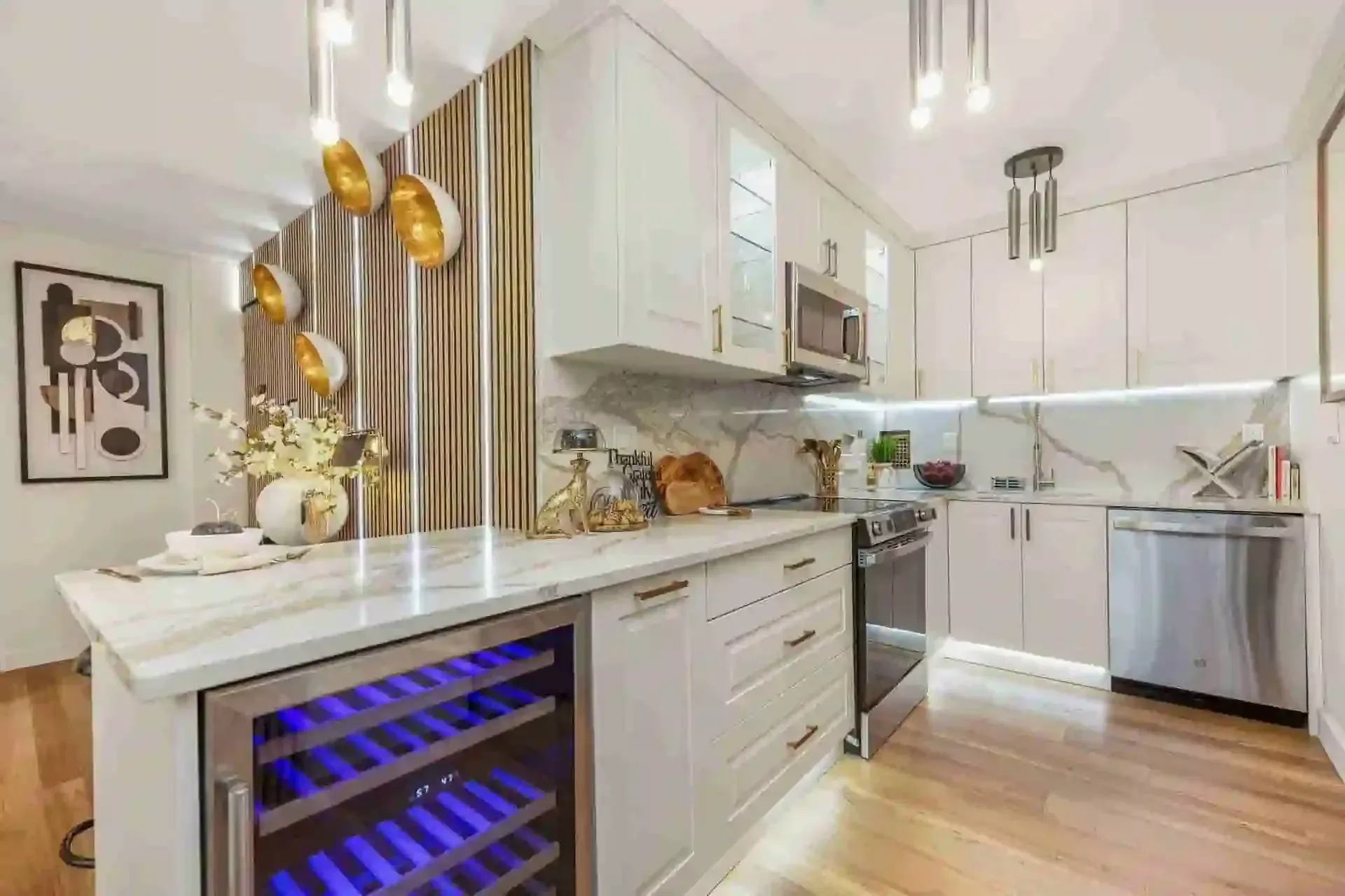 Bright modern white kitchen with marble island, gold pendants, and blue-lit wine cooler