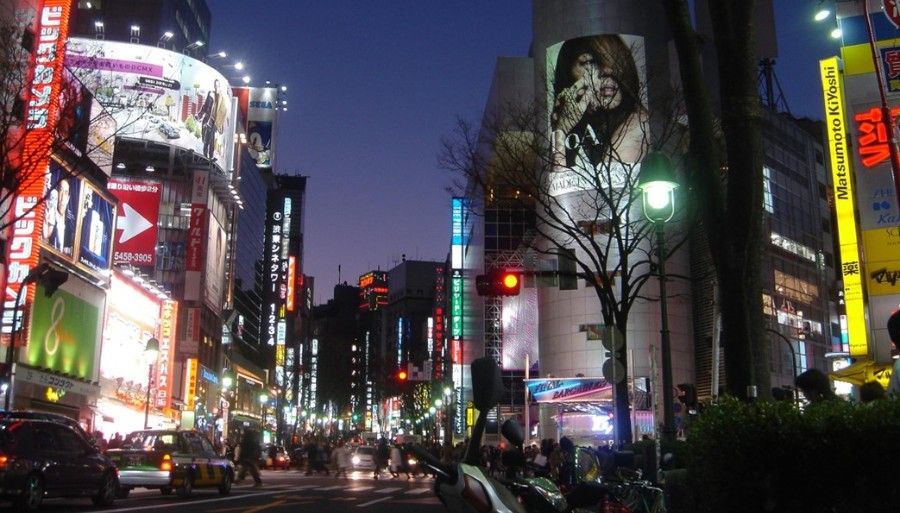 Shibuya street at night with a sign that says ' nintendo ' on it.