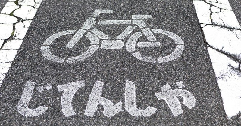 Bicycle lane marking with Japanese text painted on cracked white pavement