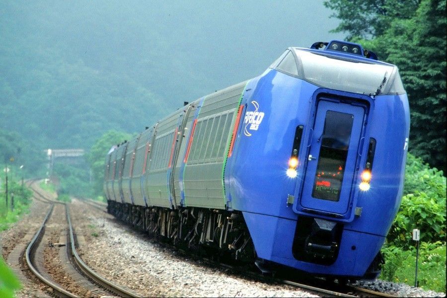 Blue train leaning into a curve on tracks through a green, misty hillside