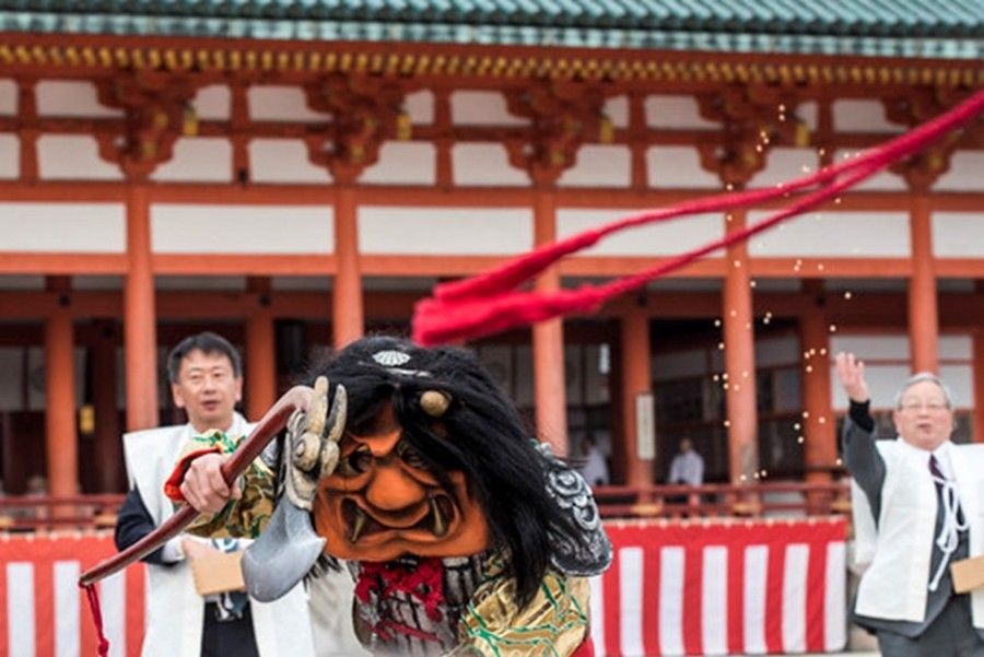 Person in mask throwing beans at a Japanese temple during a festival.