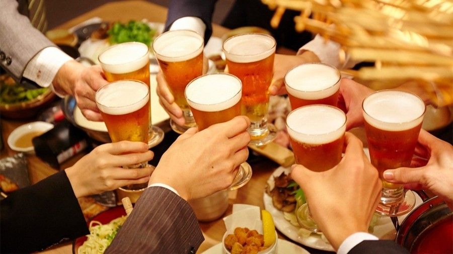 People toasting with beer glasses at a table, various food items present.