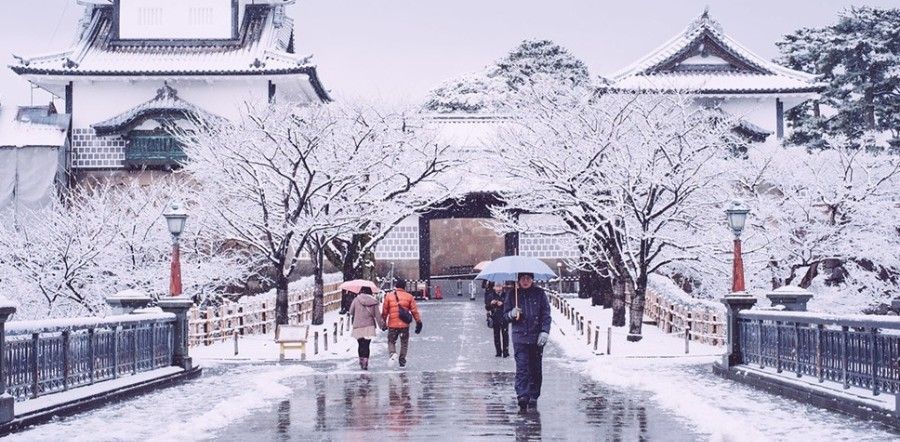 A group of people walking in the snow with umbrellas at Kanazawa Castle.