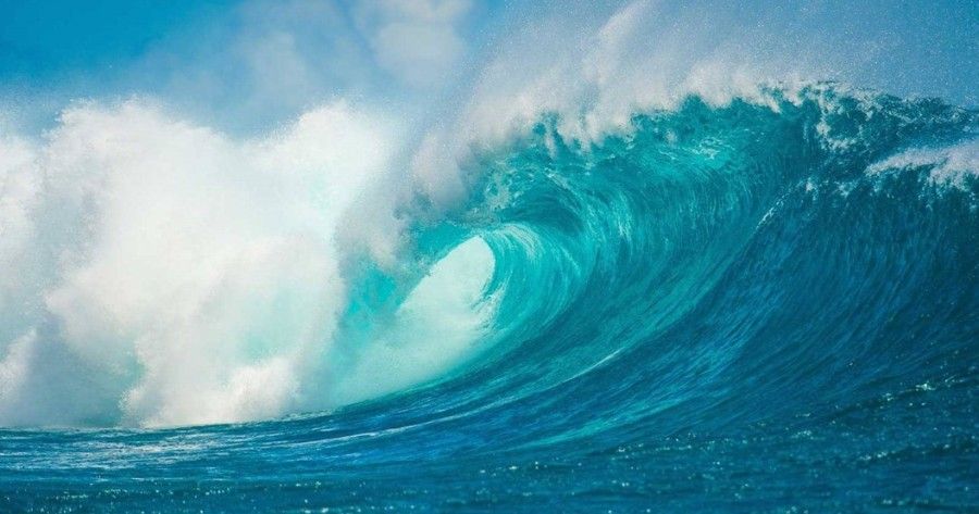 A large wave in the ocean with a blue sky in the background.