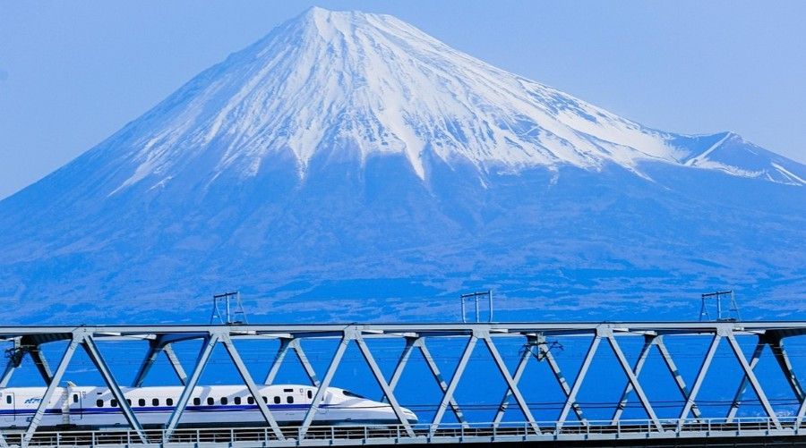 A bullet train is going over a bridge with Mt. Fuji in the background.