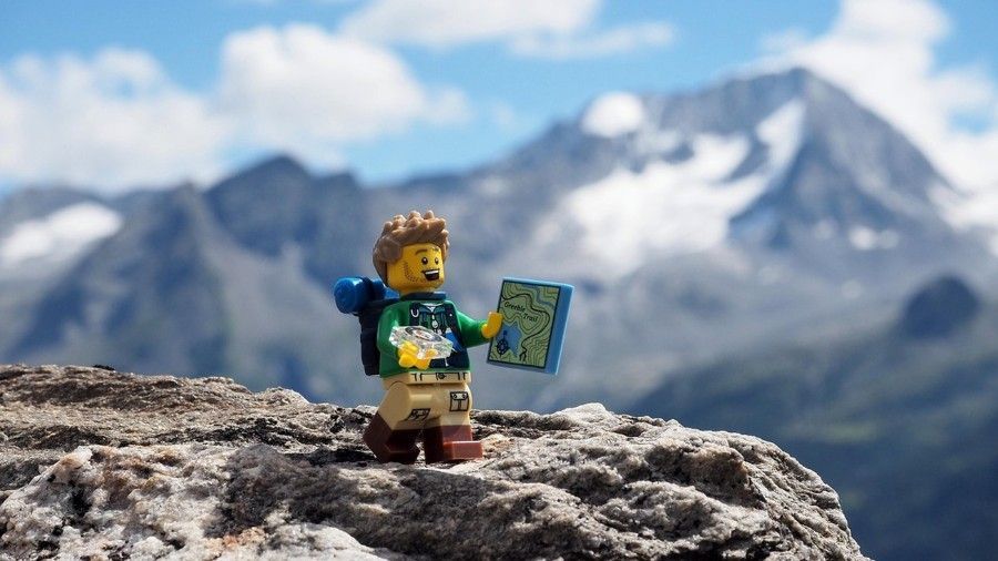 A Lego man is standing on top of a mountain holding a map.