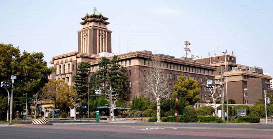A large building with a tower on top of it is surrounded by trees and a street.