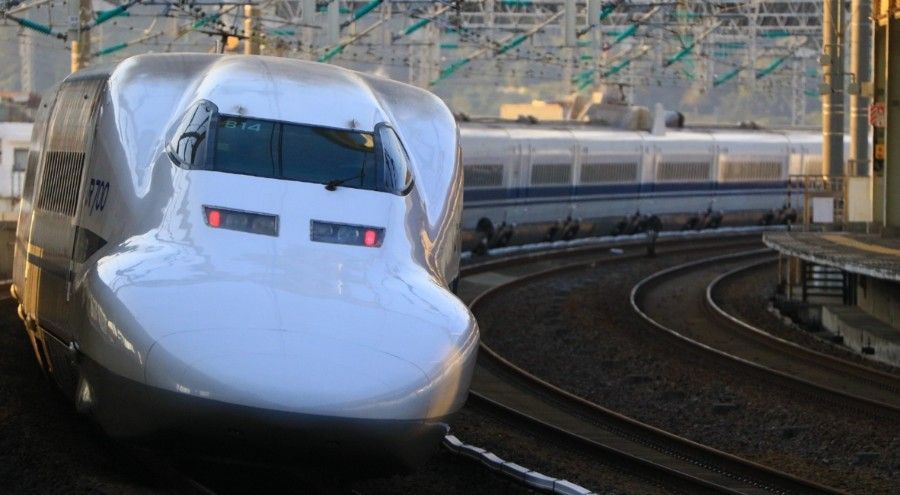 A sleek, white bullet train curving on tracks at a station in Japan.