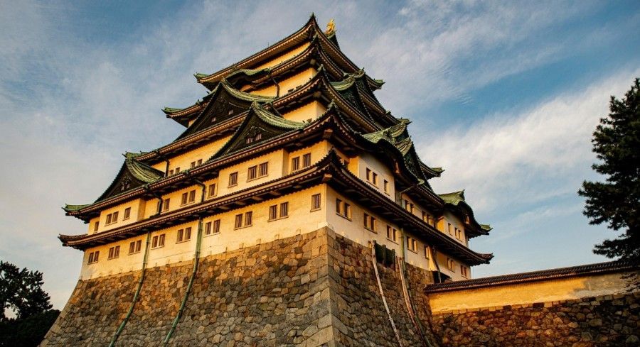 Nagoya Castle, Japan, with white walls, green tiled roof, and stone base under a blue sky.