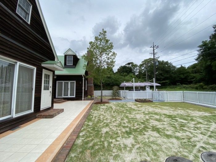 Wooden house in Nagoya, Japan with a white picket fence surrounding a grassy yard under a cloudy sky. Perfect for a pet to play in.