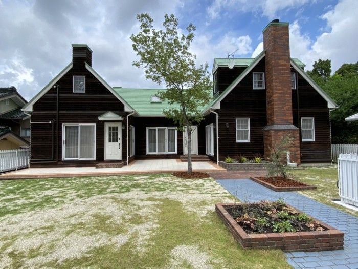 A dark brown house with a green roof and brick chimney, centered by a small tree, with a grass lawn. Pet-friendly home in Nagoya. Japan.