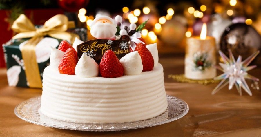 Christmas cake with strawberries and Santa decoration on a table with gifts and candles.