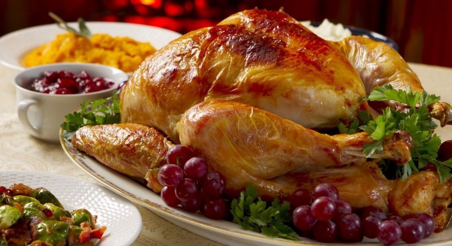 Roasted turkey on a platter with grapes and cranberry sauce, mashed sweet potatoes and other sides.