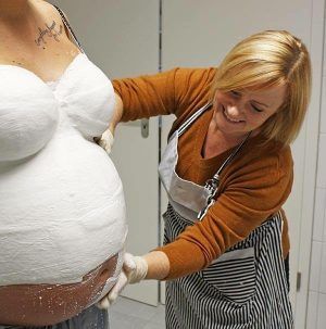 A woman is plastering a pregnant woman 's belly.