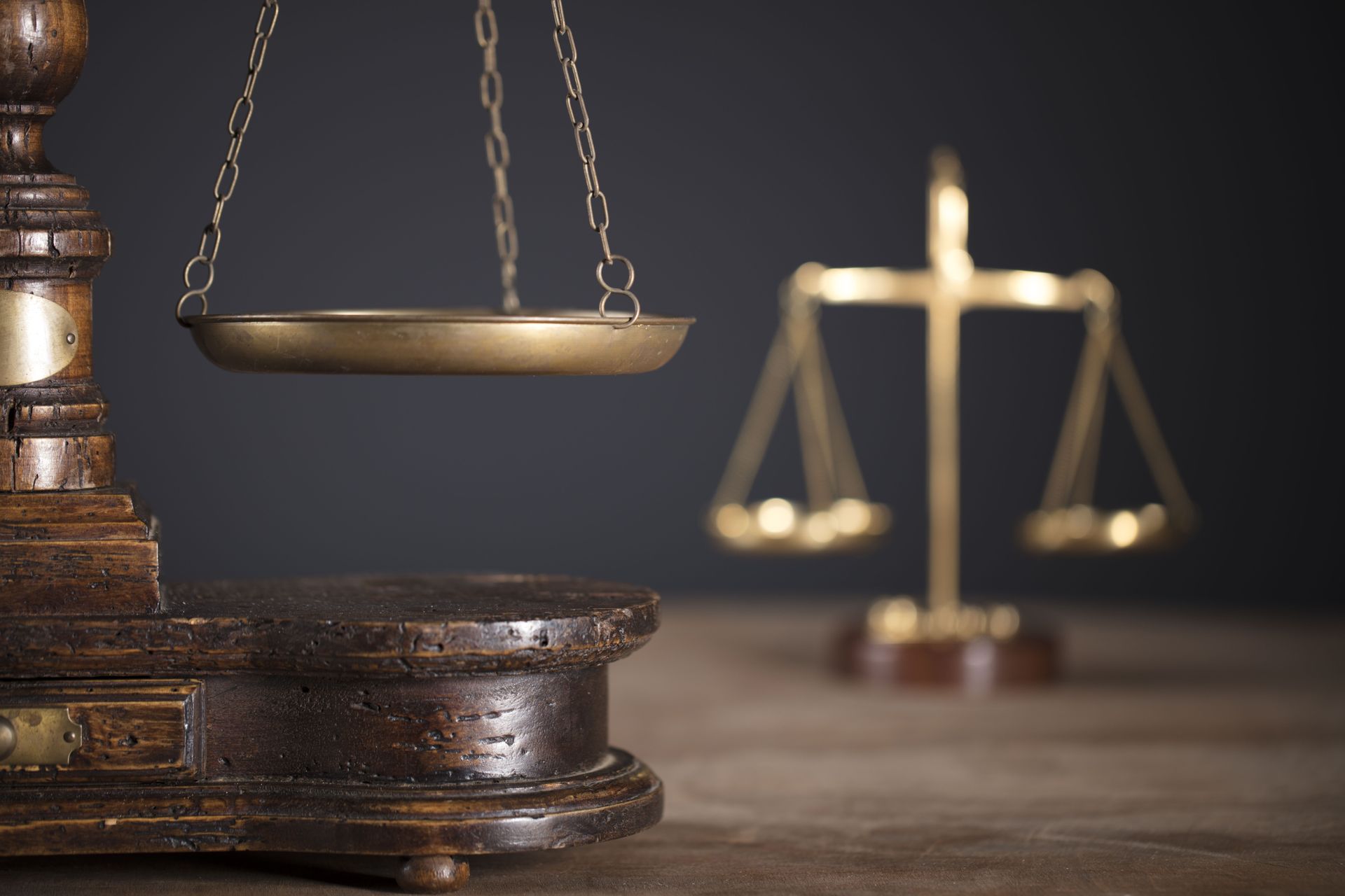 Close-up of a wooden balance scale with brass pans in focus; another scale is blurred in the background.