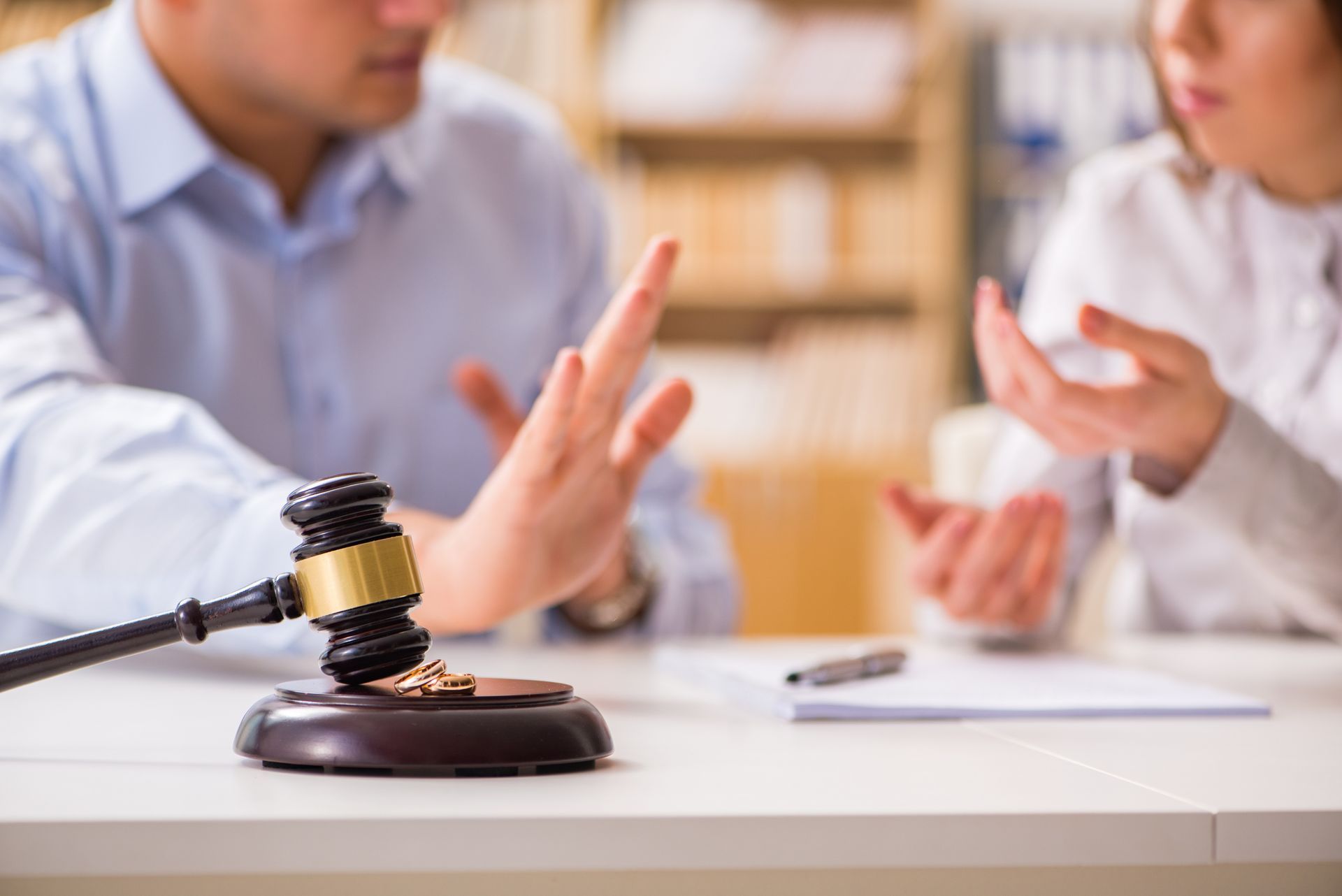 Divorce proceeding: Couple argues near a gavel and wedding ring on a desk.