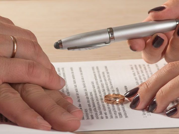 Hands with wedding rings, signing divorce papers, one hand holds pen.