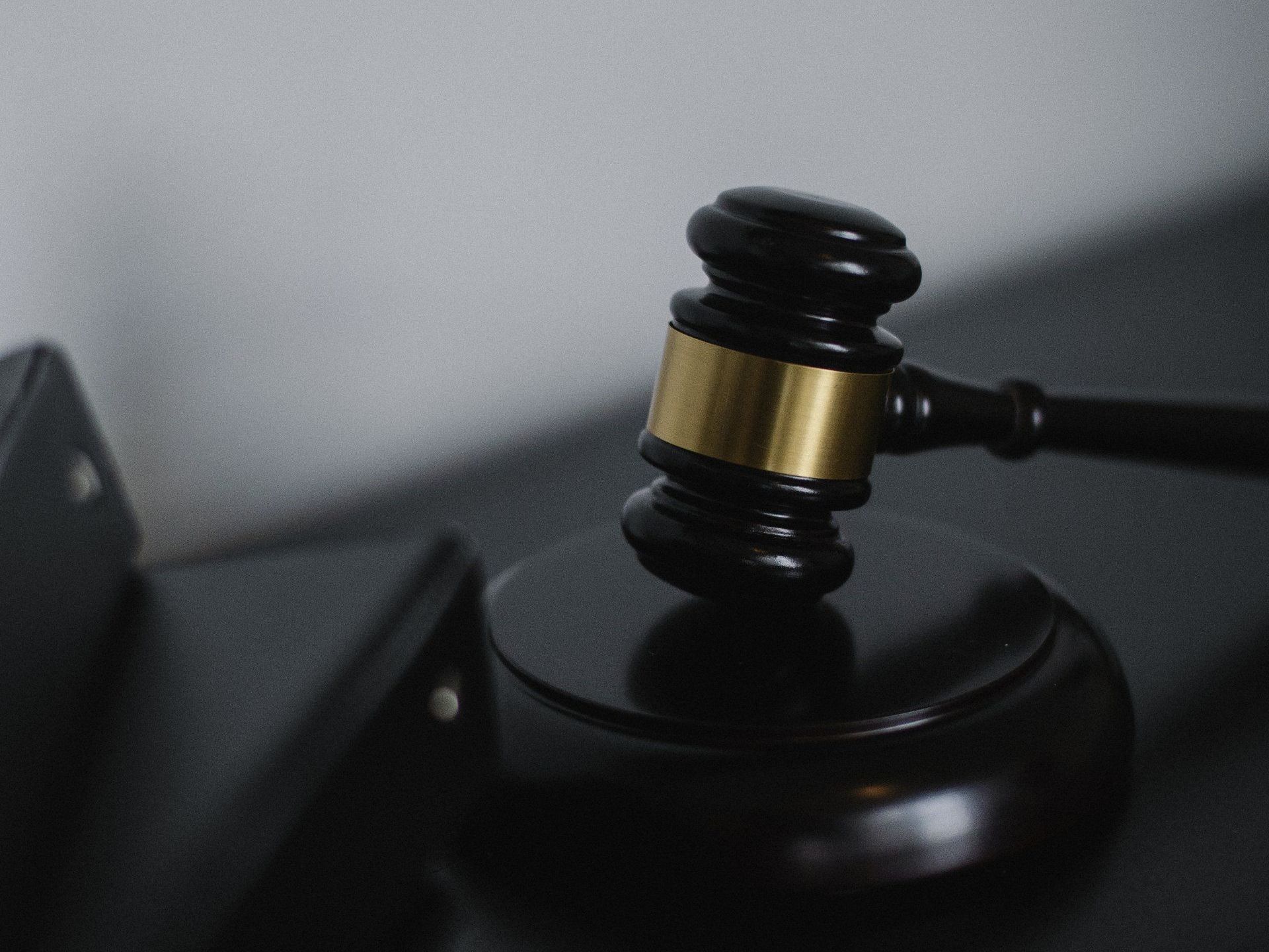 Close-up of a wooden gavel with a brass band resting on its sound block, suggesting a courtroom or legal setting.