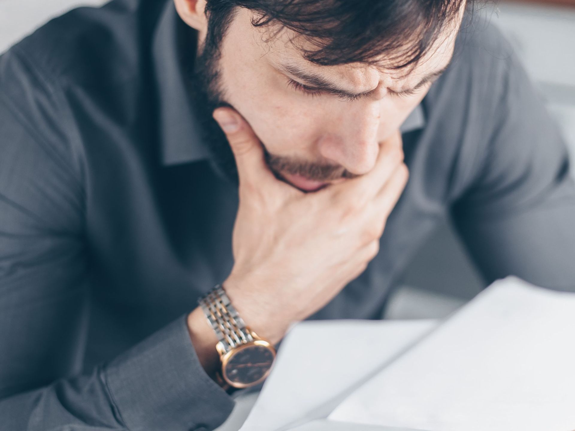 Man with beard, furrowed brow, and hand on chin, looking at documents.
