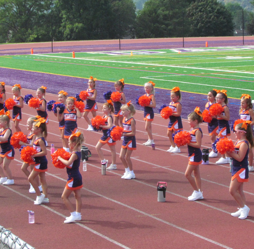 Cheerleader in red uniform performs a backbend on a green and red football field.