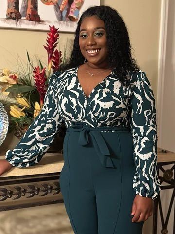 A woman in a green and white jumpsuit is standing next to a table.