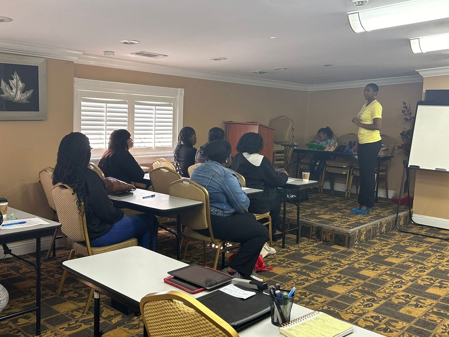 A group of people are sitting at tables in a room while a man gives a presentation.