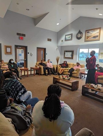 A woman is standing in front of a group of people sitting on couches in a living room.