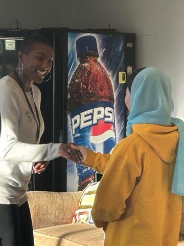 Two women are shaking hands in front of a pepsi vending machine.