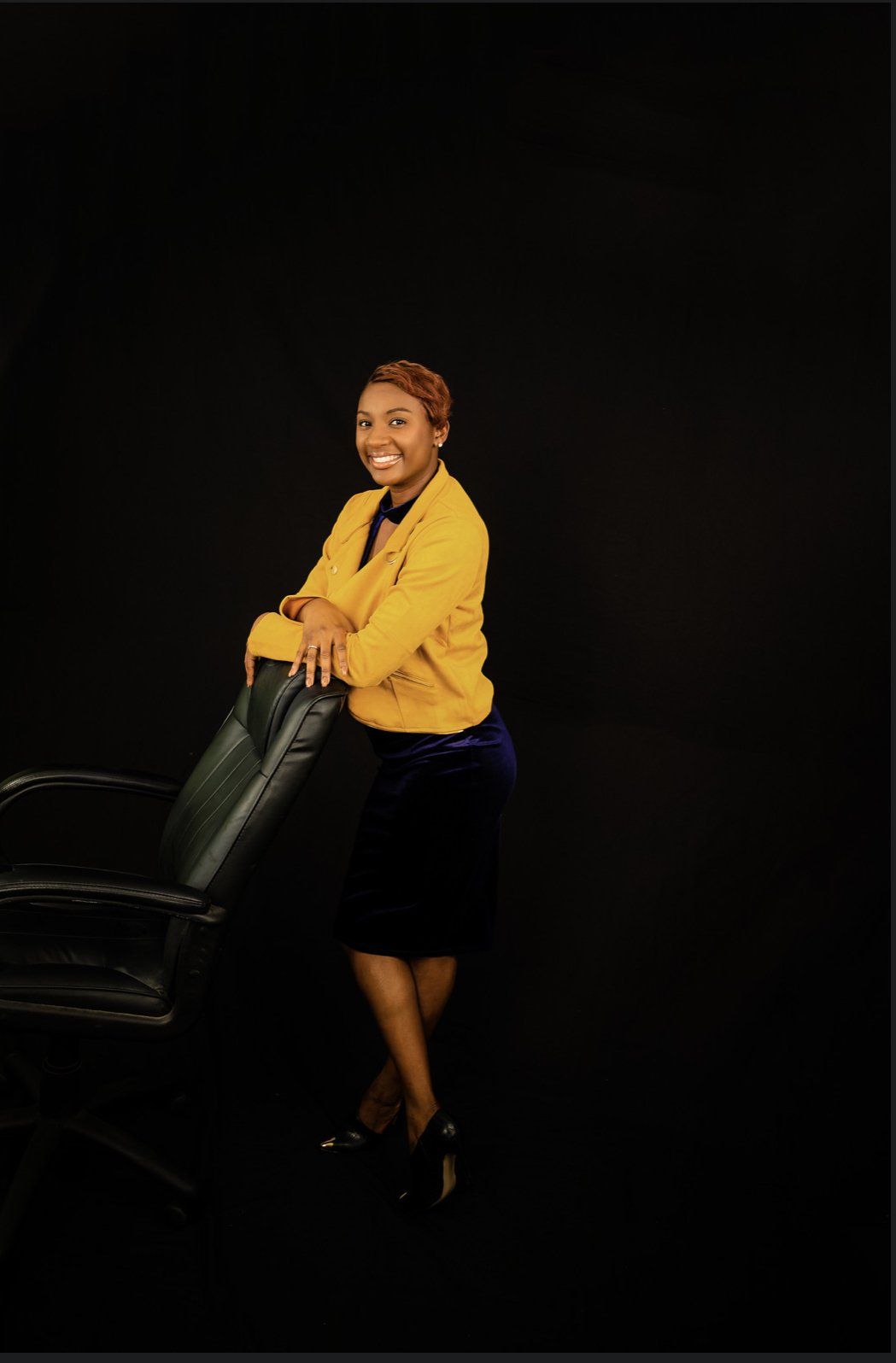 A woman in a yellow jacket is leaning on a chair.