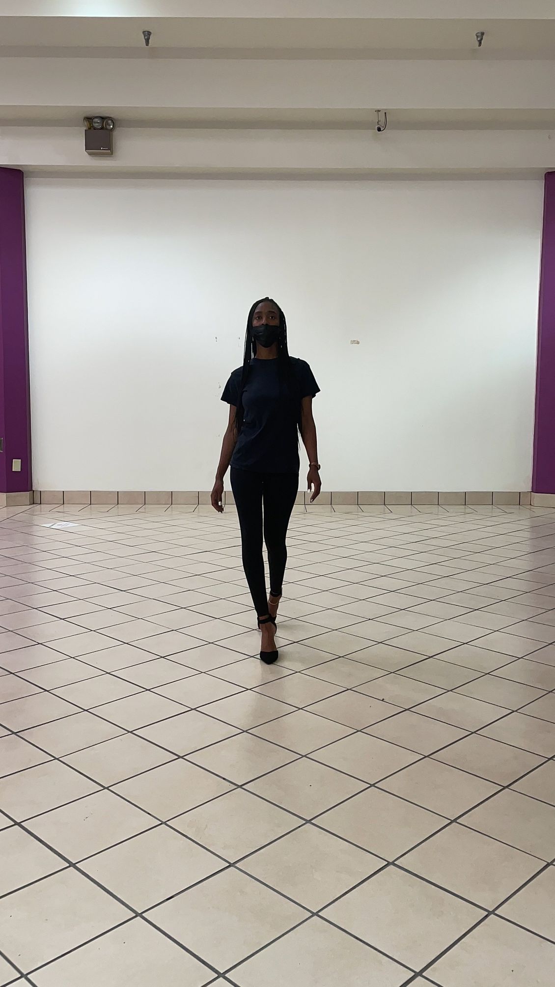 A woman is walking in an empty room with a checkered floor.