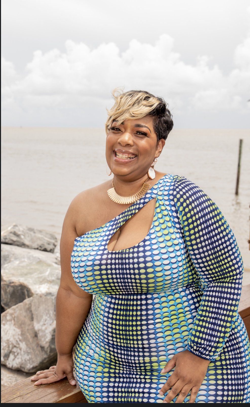 A woman in a blue and green dress is standing next to a body of water.