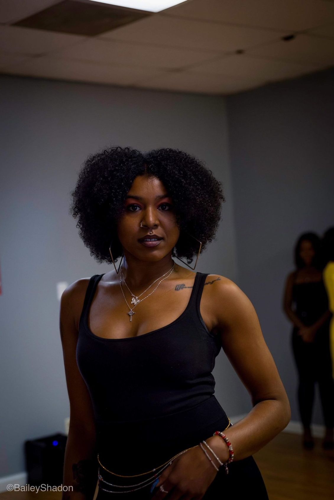 A woman in a black tank top is standing in a room.