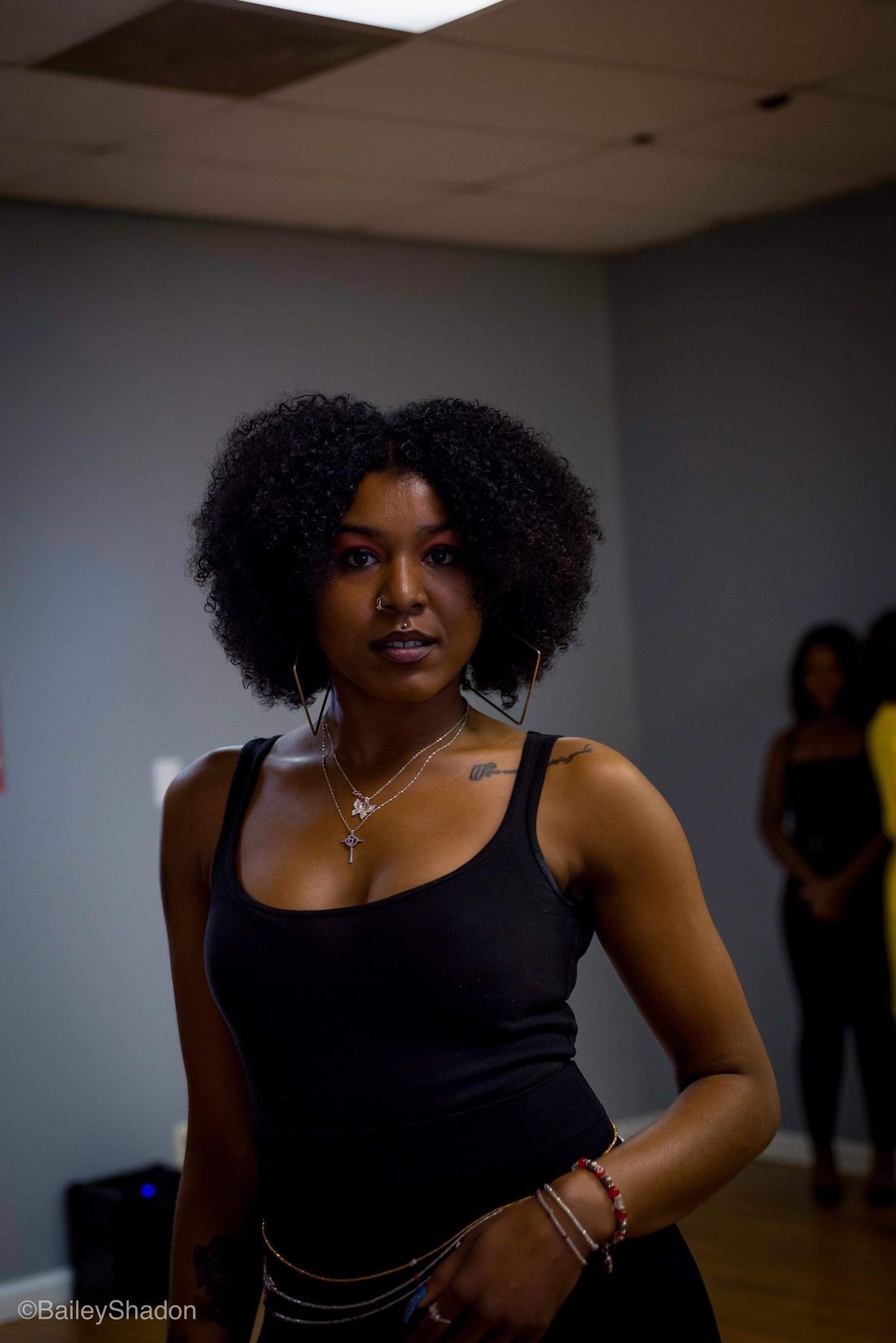 A woman in a black tank top is standing in a room.