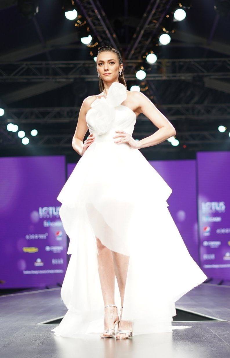 A woman in a white dress is walking down a runway