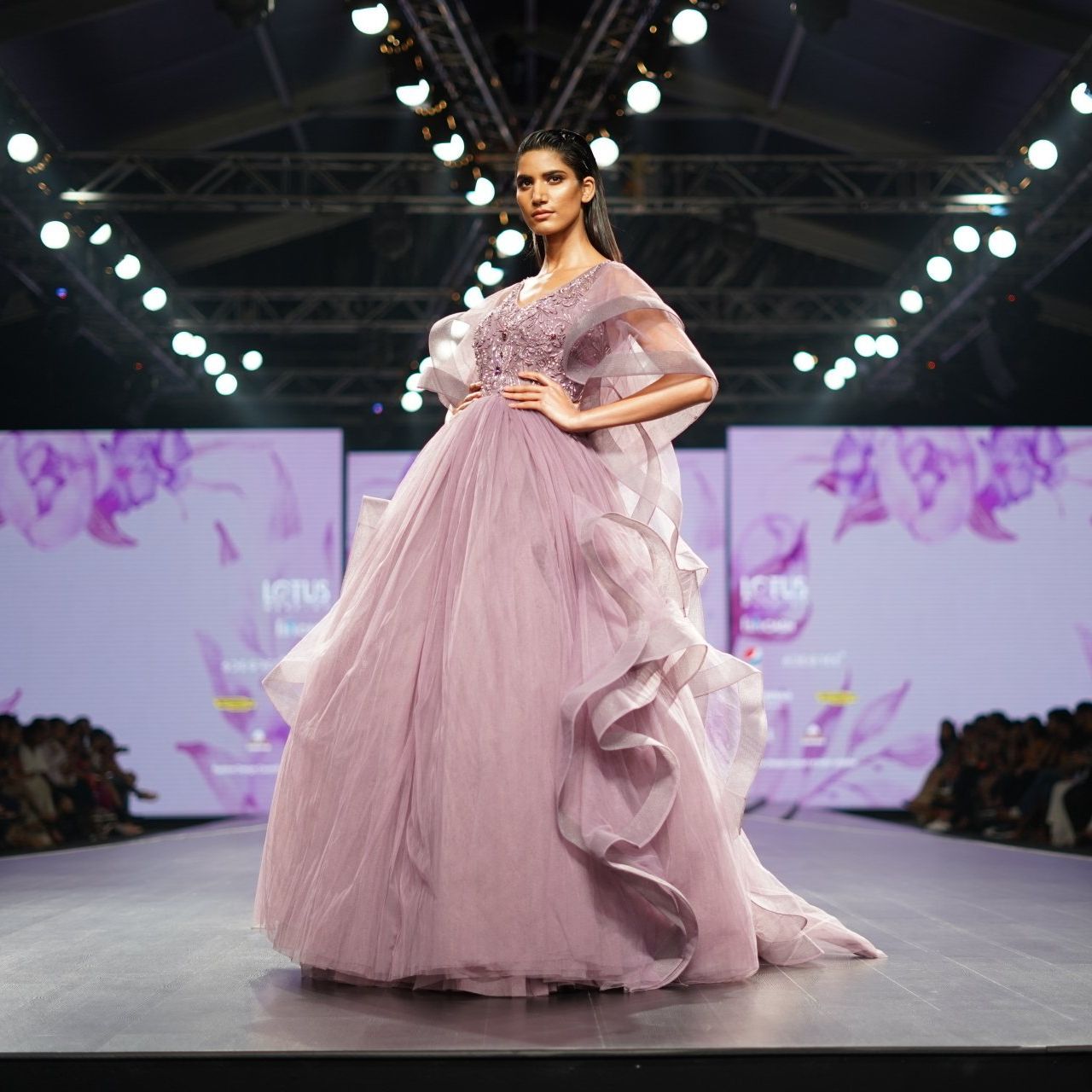 A woman in a long pink dress is walking down a runway