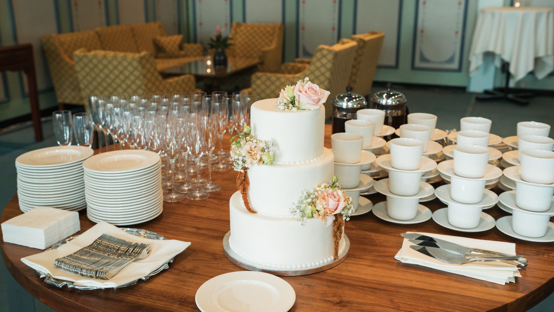 Bryllupskage og forfriskninger på et bord; glas, kopper og servietter er arrangeret.