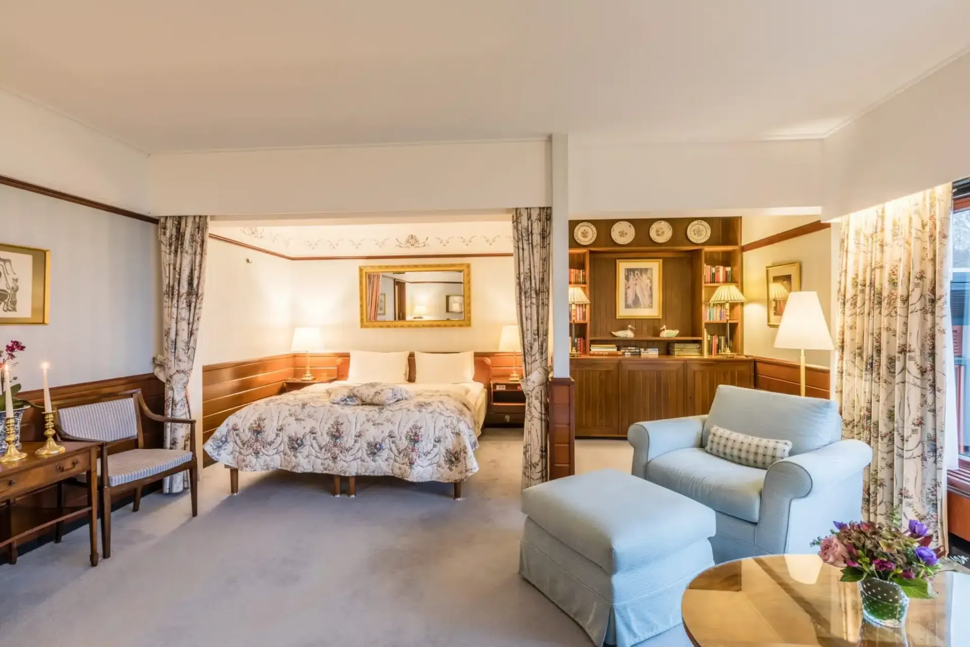 Et hotelværelse med seng, stole, skammel og bord.