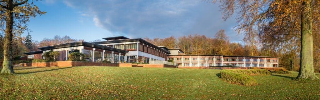 En stor bygning ligger midt i en frodig grøn mark omgivet af træer.