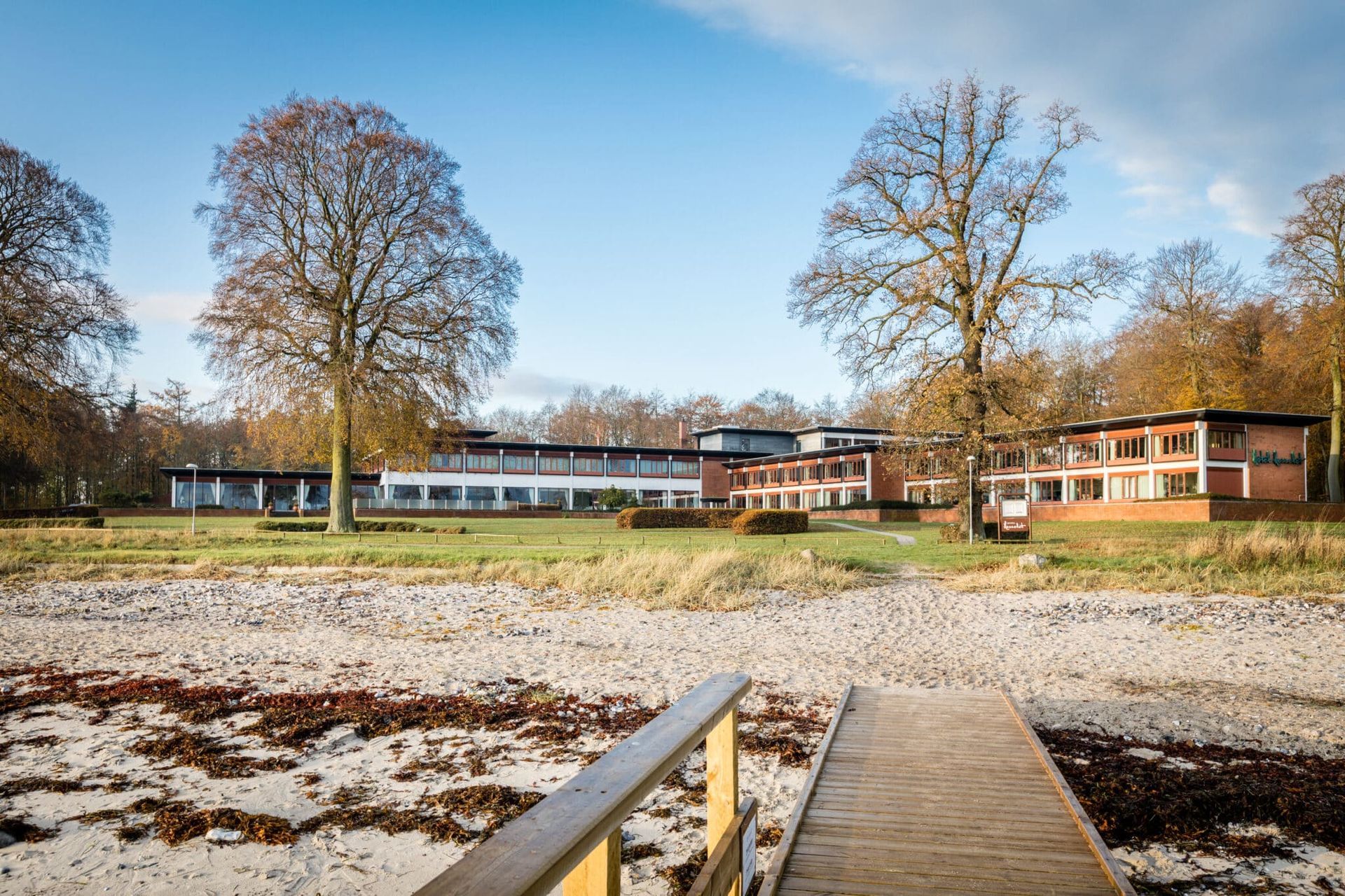 Borddækning med frugt, vandflasker, glas og notesblokke på et hotelværelse med lænestole.